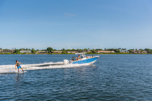 Wakeboarder being towed behind blue and white center console boat near residential waterfront