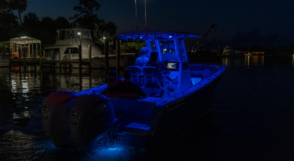 Blue-lit center console fishing boat docked at a marina at night with palm trees and lit dockside structures in background