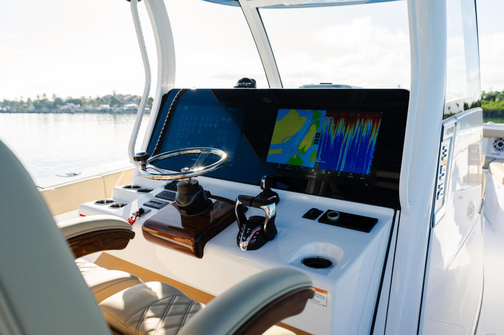 Helm station with dual monitors displaying sonar and navigation data, steering wheel, and control console overlooking calm water