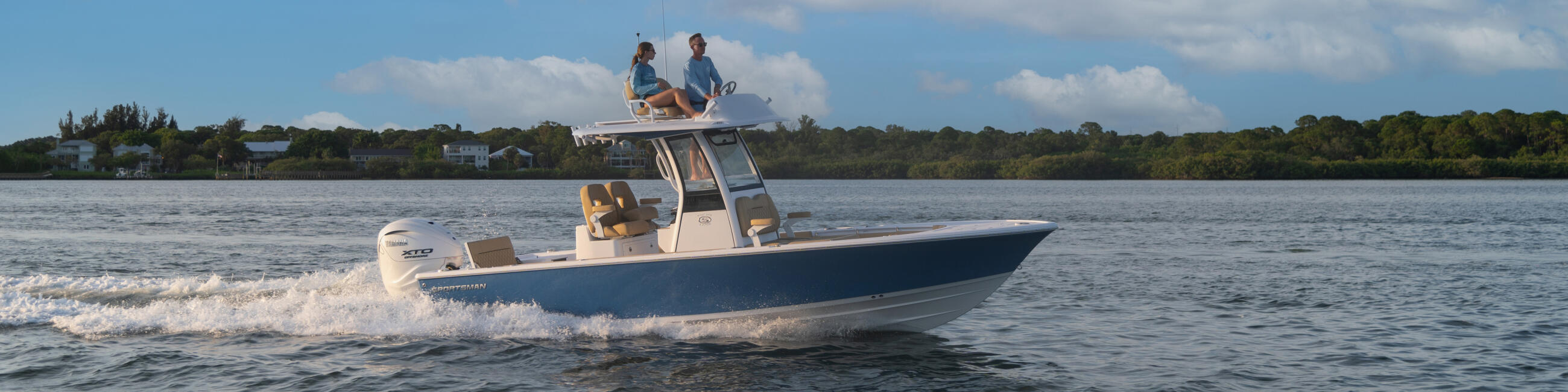 Couple enjoying a Masters bay boat running through shallow coastal waters with scenic shoreline in background