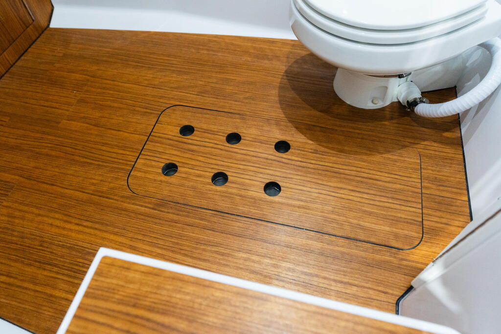 Cabin sole with six through-hull drain holes and white toilet installed