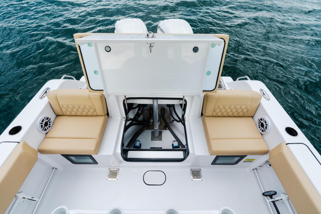Overhead view of boat deck with tan cushioned seating, center console with engine access, and calm turquoise water