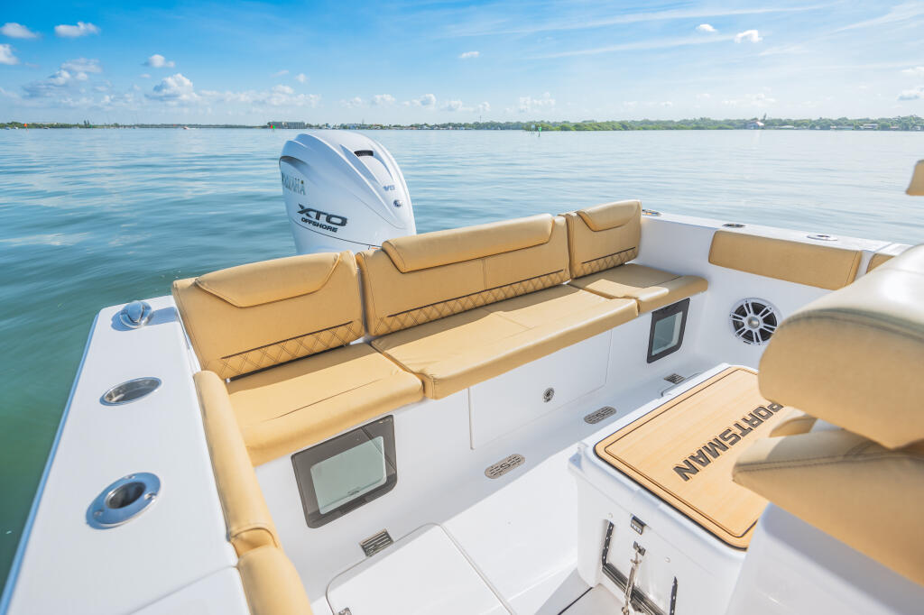 Tan cushioned seating with storage in the rear of a white center console boat with outboard motor on calm blue water