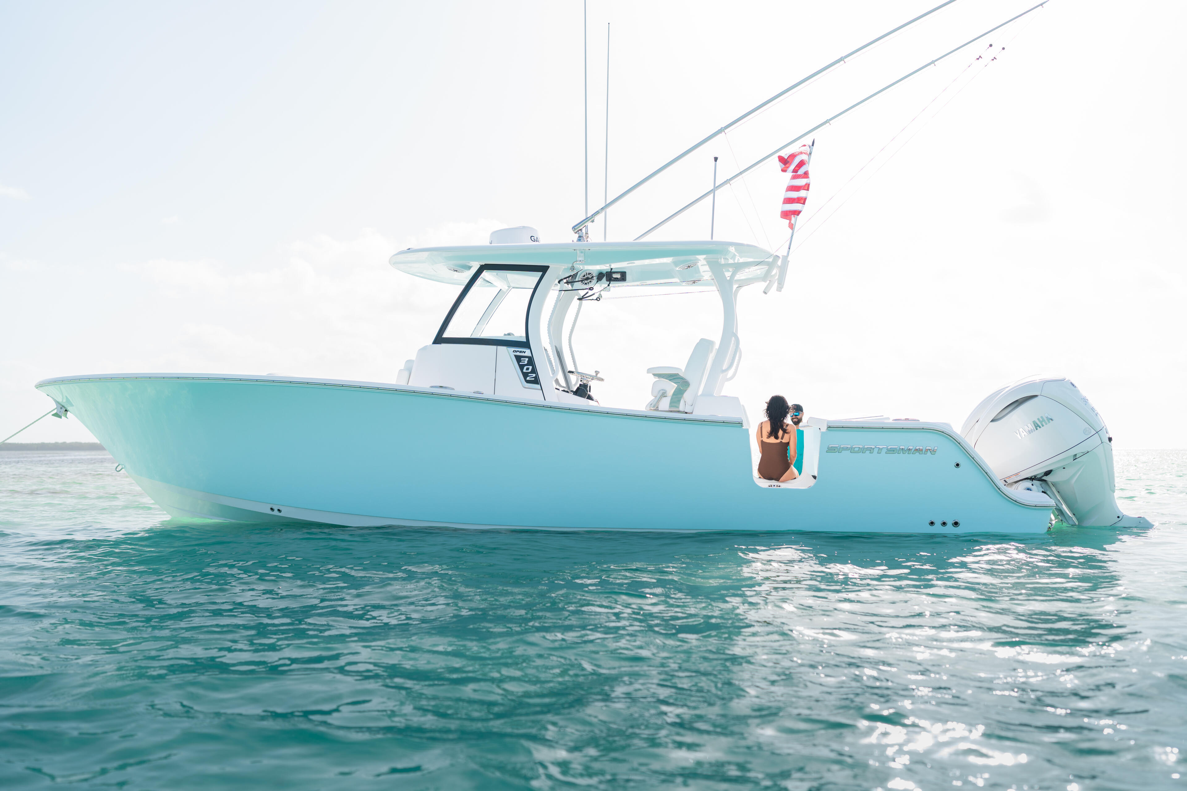 Turquoise boat anchored in shallow water with a woman relaxing onboard near the beach