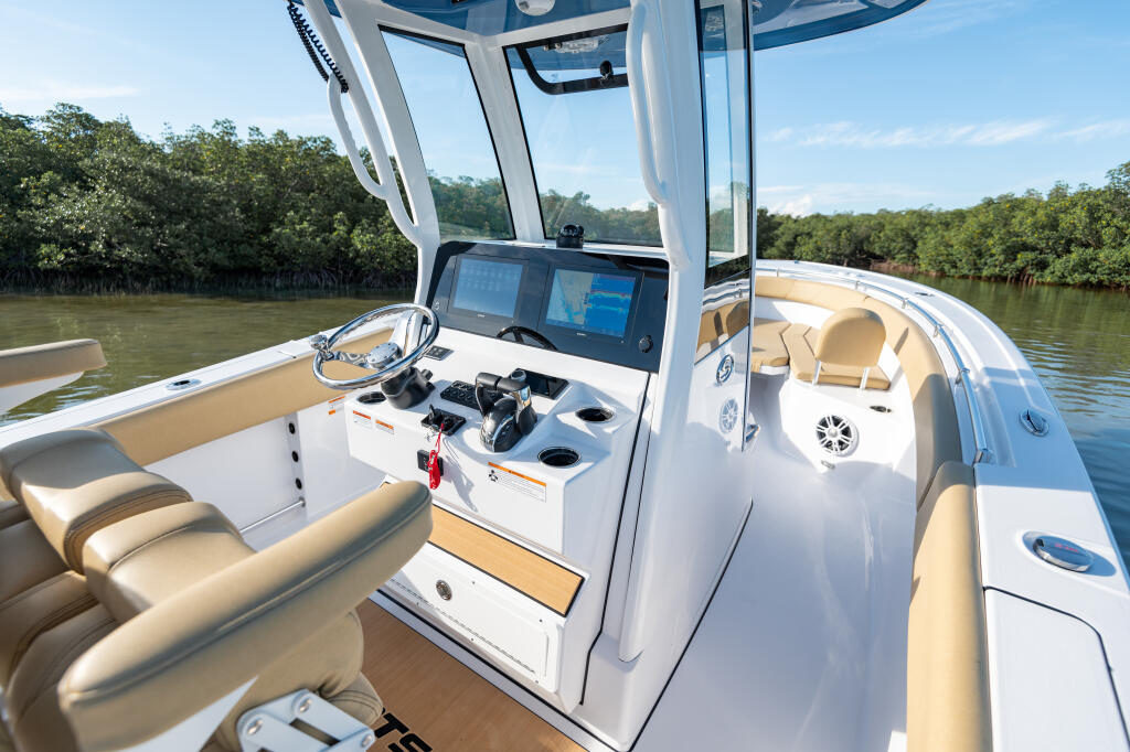 Center console helm with dual monitors, tan seating, and hard-top canopy overlooking calm mangrove waters