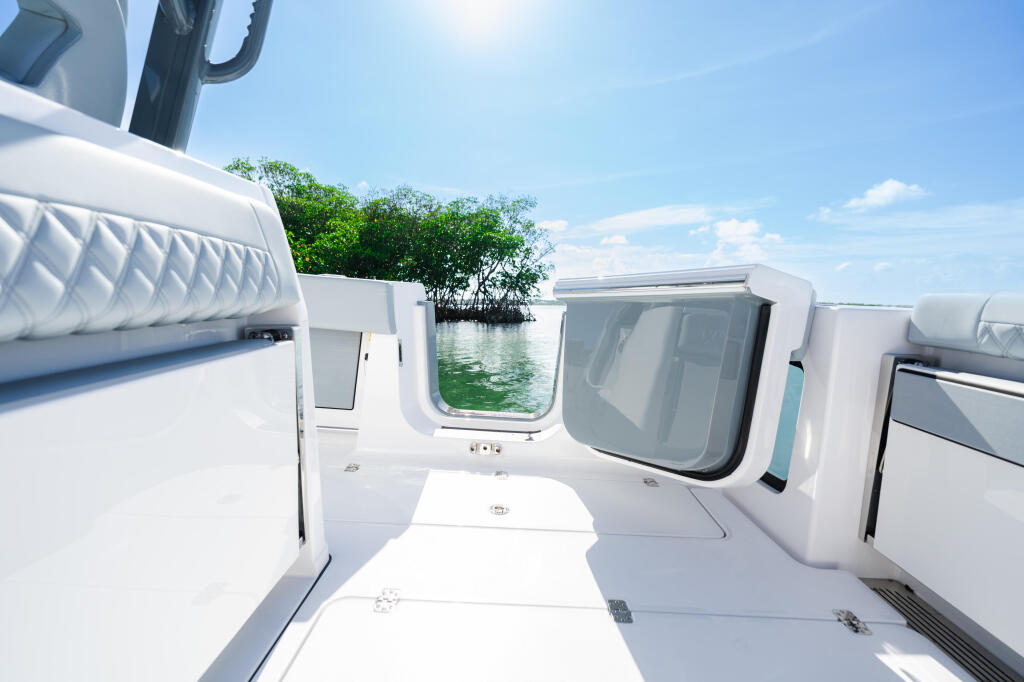 Open cabin area with seating, windows overlooking mangrove shoreline and calm water