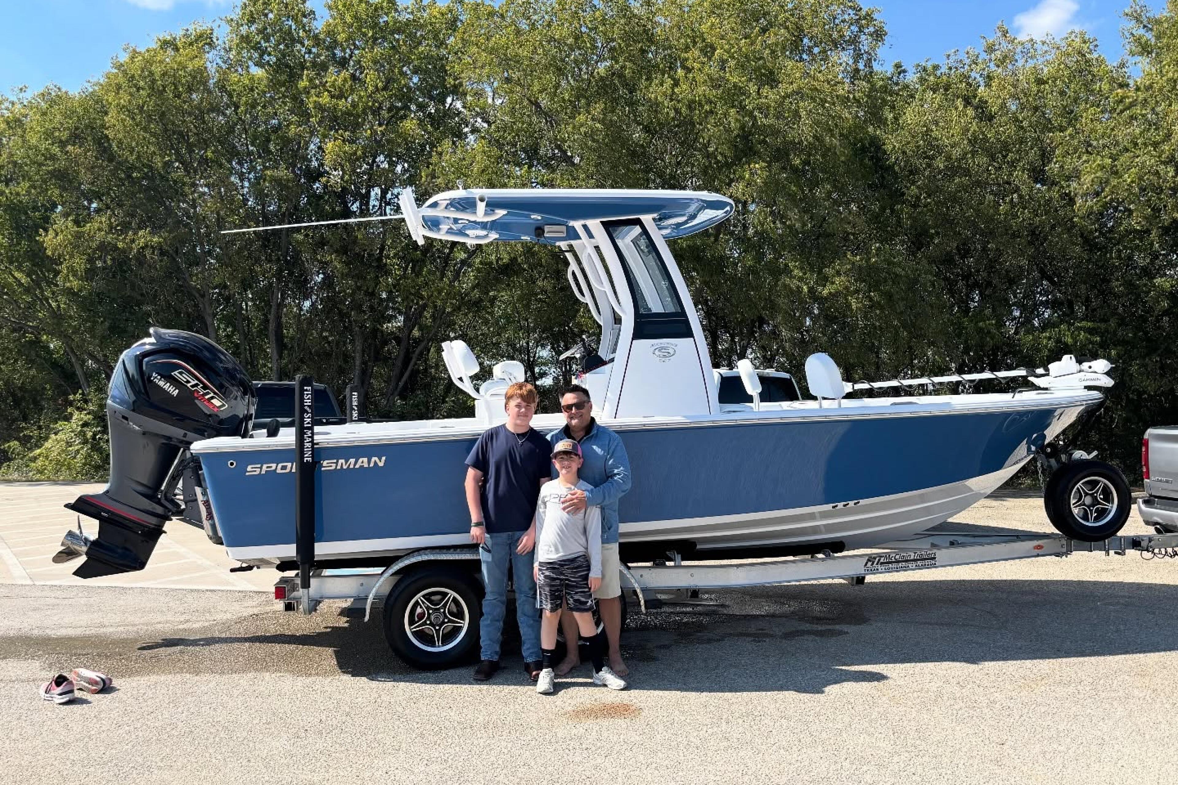 Family of three posing in front of a blue and white Sportsman boat on a trailer