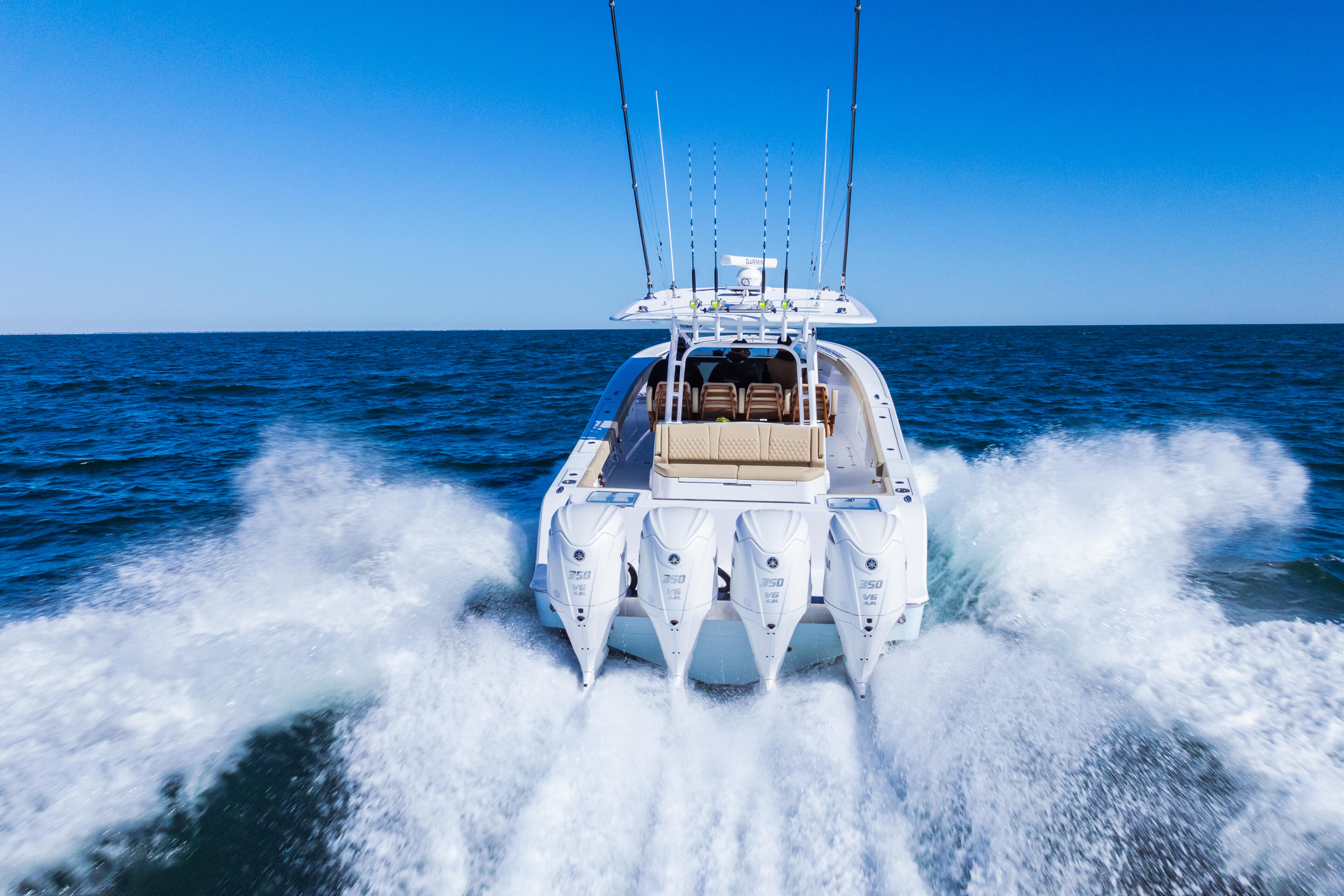 Quad-engine white sport fishing boat running at full speed through offshore waves