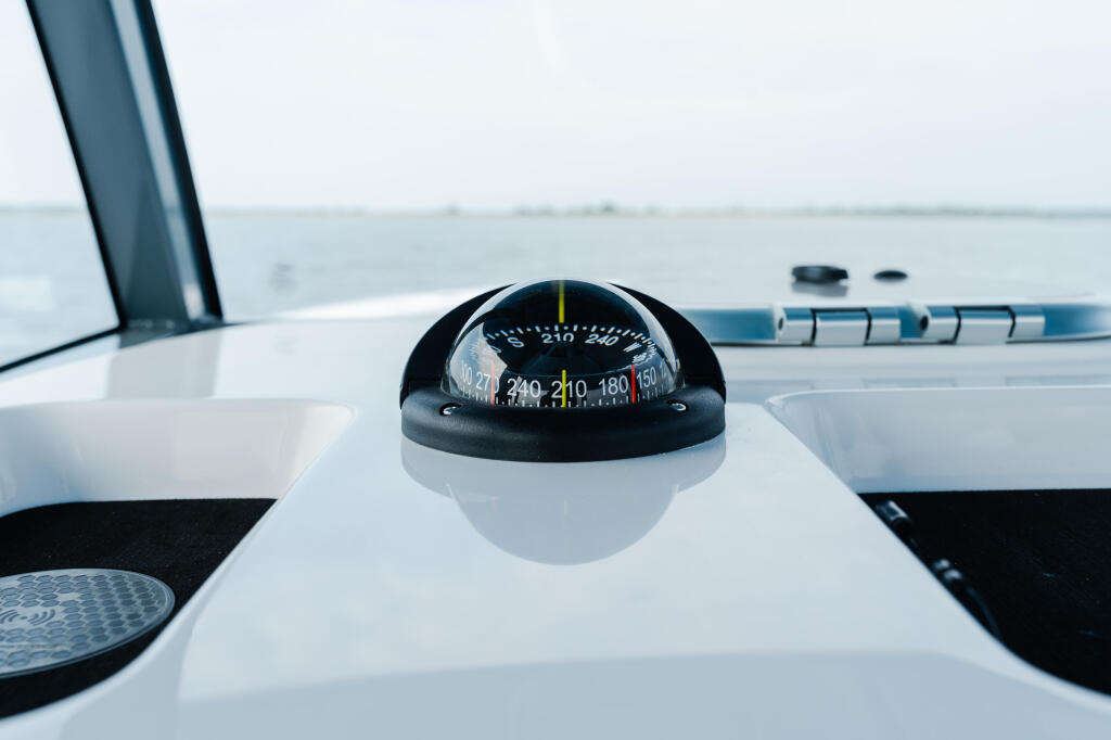 Magnetic compass mounted on boat helm dashboard with calm open water visible ahead