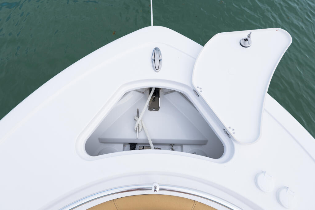 Open bow anchor locker on white center console boat with green water visible behind