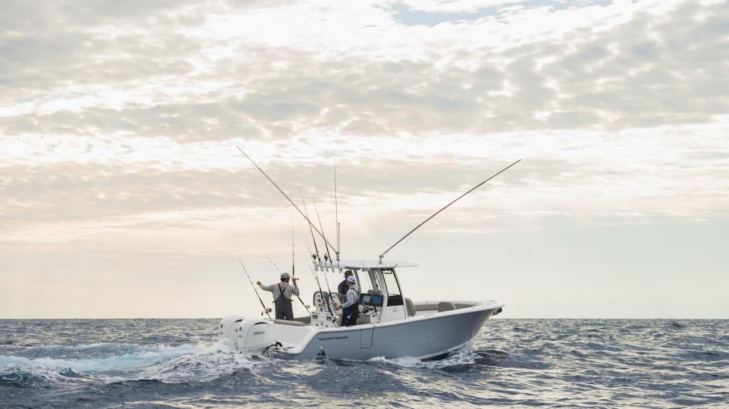 Fishing boat with anglers and multiple outrigger poles running through offshore waters