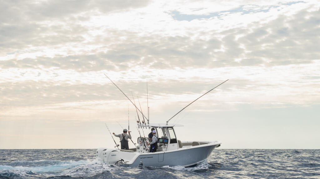 Fishing boat with anglers and multiple outrigger poles running through offshore waters