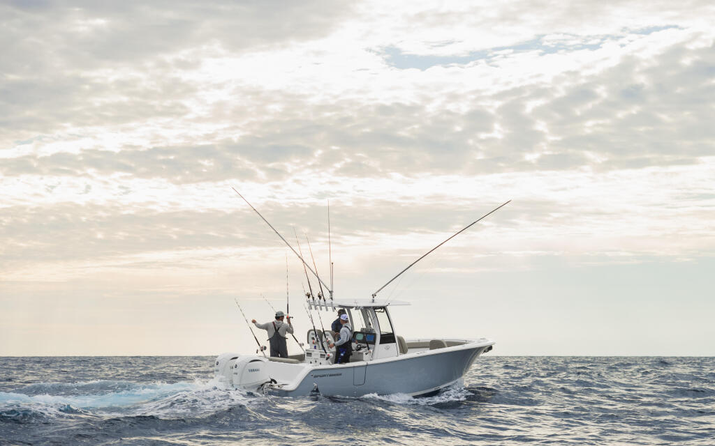 Fishing boat with anglers and multiple outrigger poles running through offshore waters