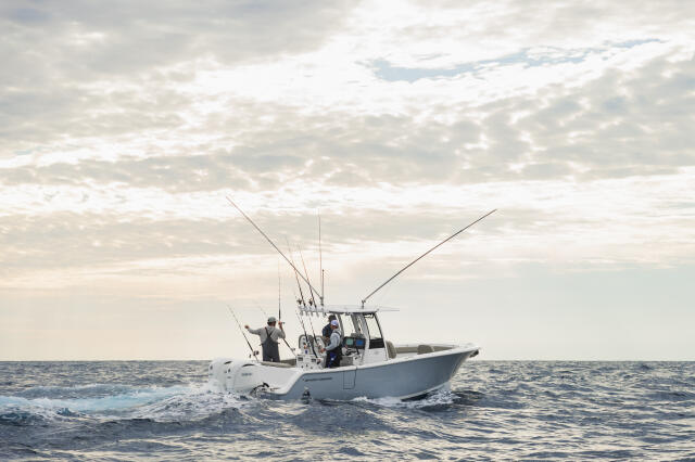 Fishing boat with anglers and multiple outrigger poles running through offshore waters