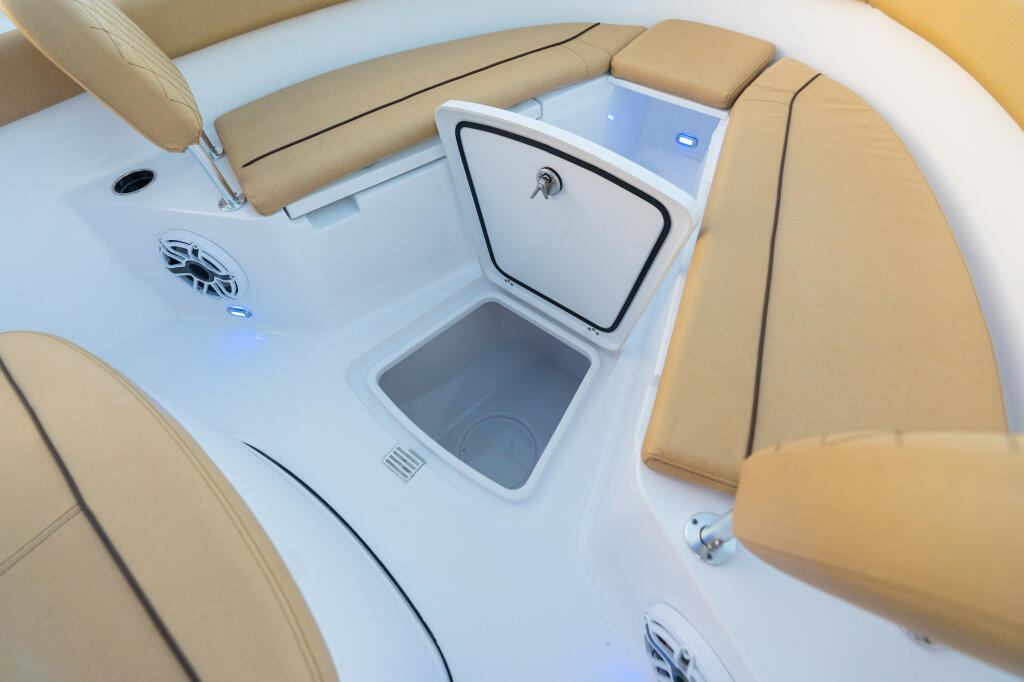 Tan upholstered seating surrounding an open white storage locker with livewell access on center console