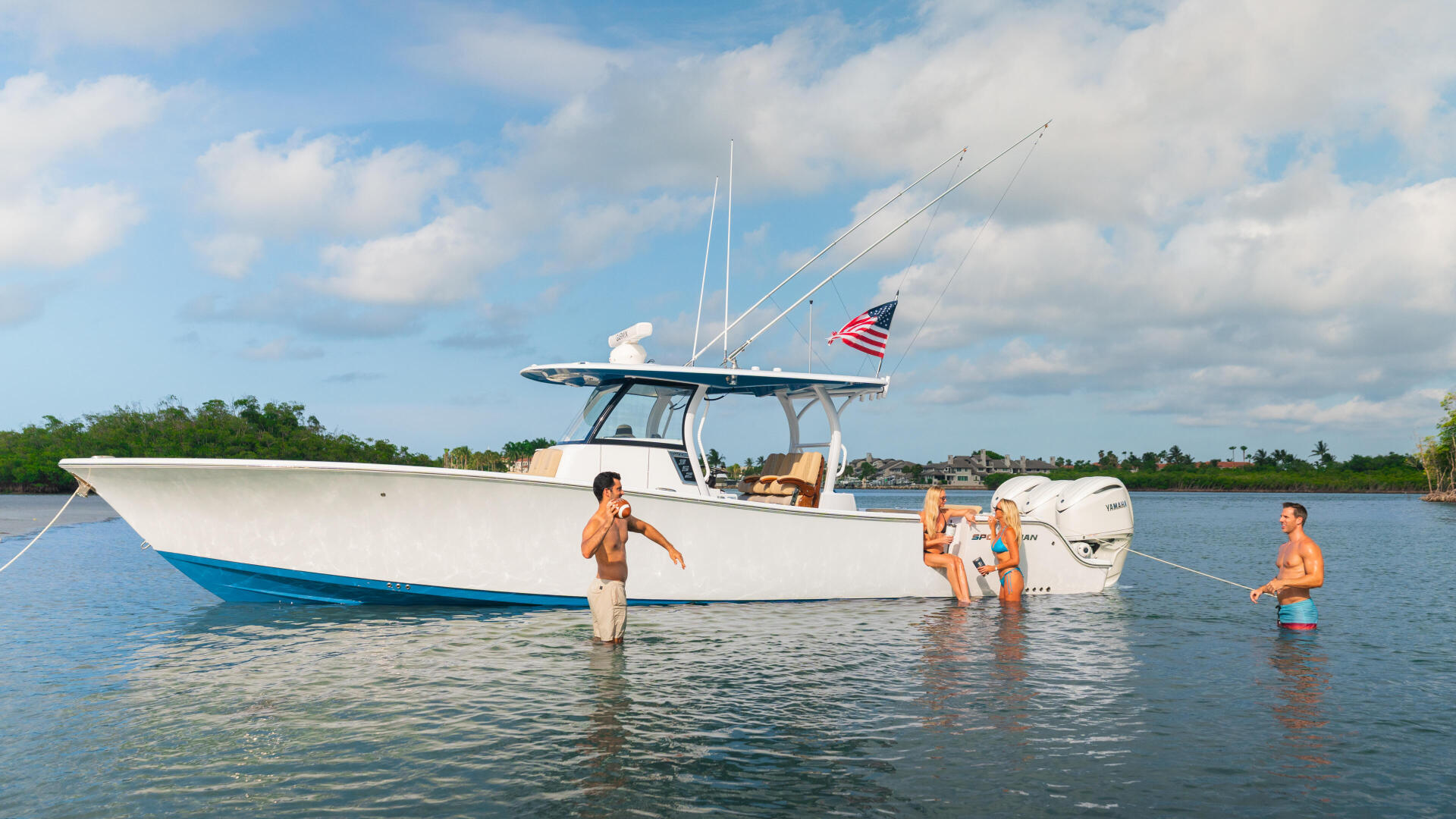 White sportfishing boat with adults and children swimming and wading in shallow turquoise water near a sandbar