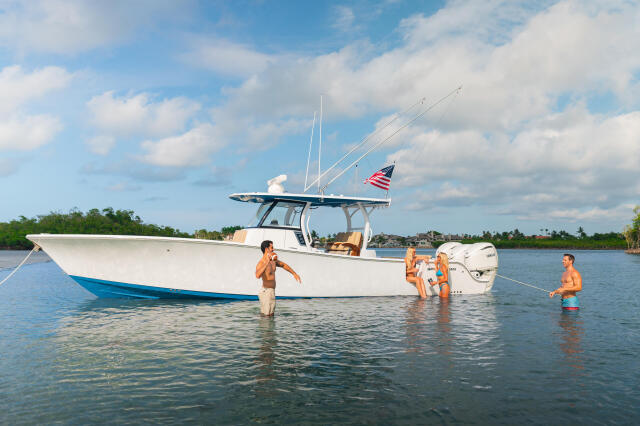 White sportfishing boat with adults and children swimming and wading in shallow turquoise water near a sandbar