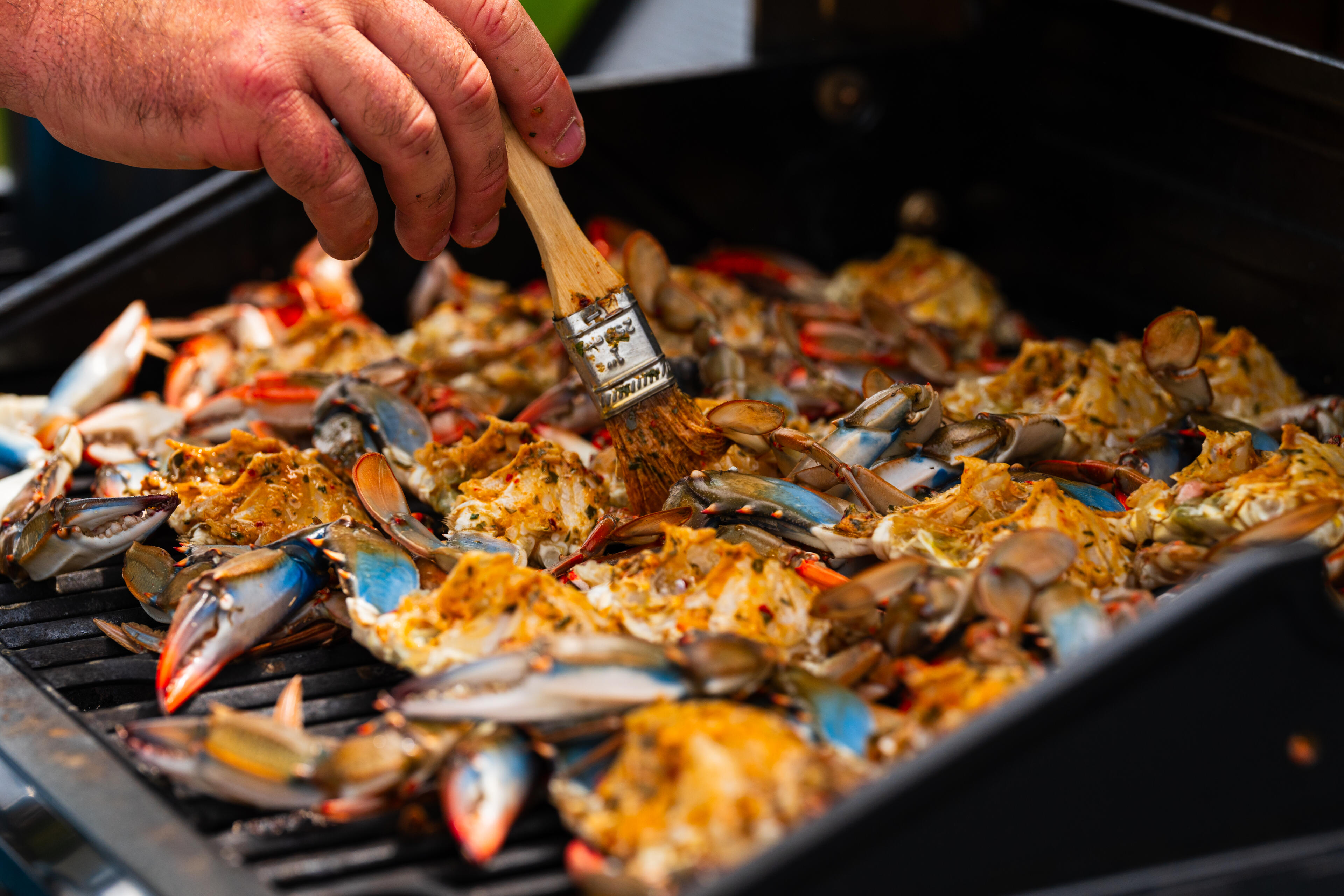 Hand brushing seasoning onto chargrilled blue crabs on a black smoker grill
