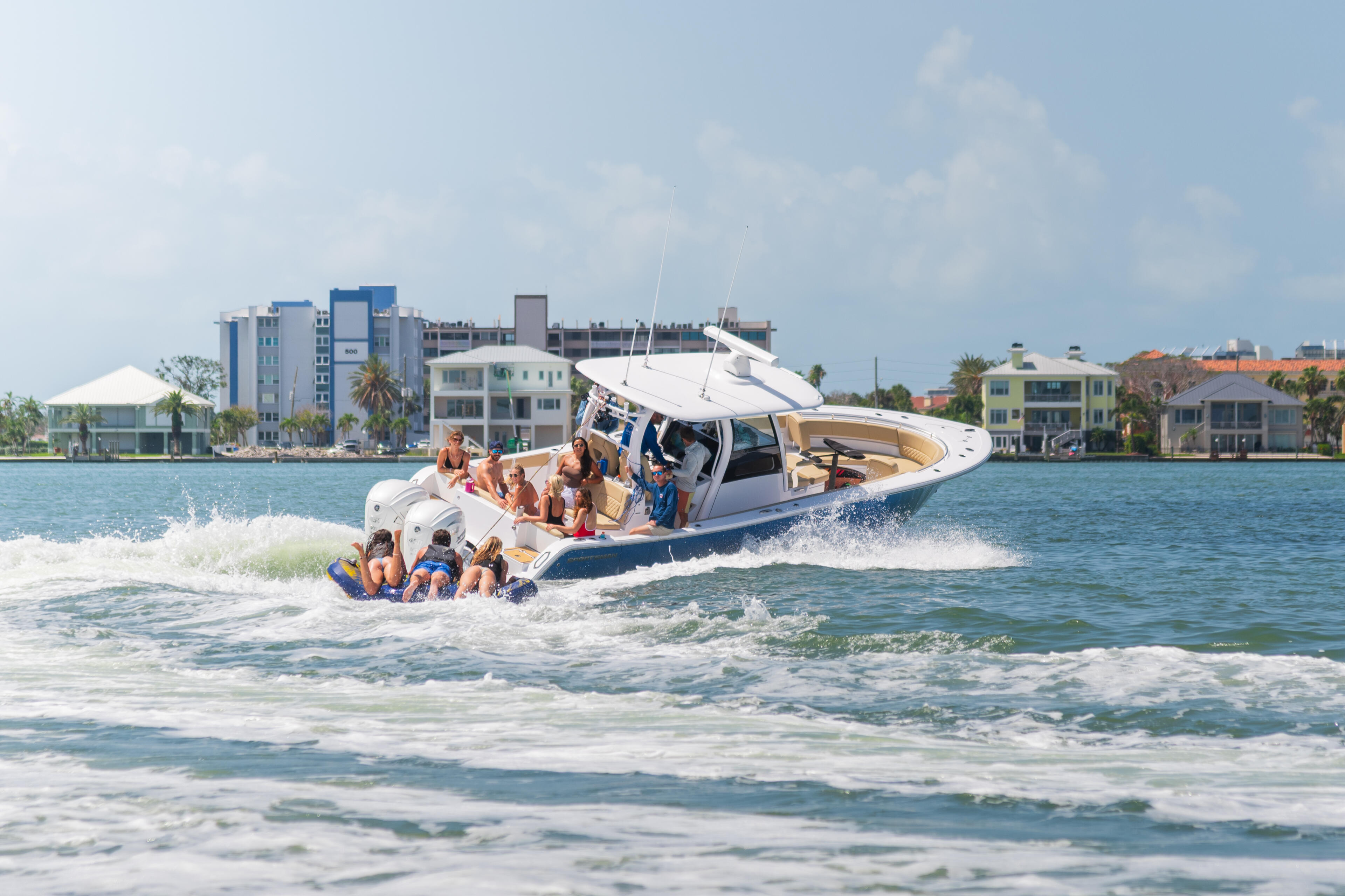 Family and friends enjoying a boat excursion in shallow waters near a sandy beach with waterfront homes in background