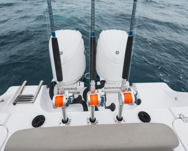Three fishing reels with orange spools mounted on the transom of a sport fishing boat, positioned above the ocean