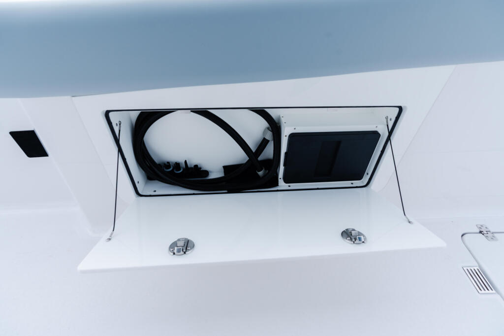 White boat cabin with open hatch showing coiled rope and fender storage, clear sky above