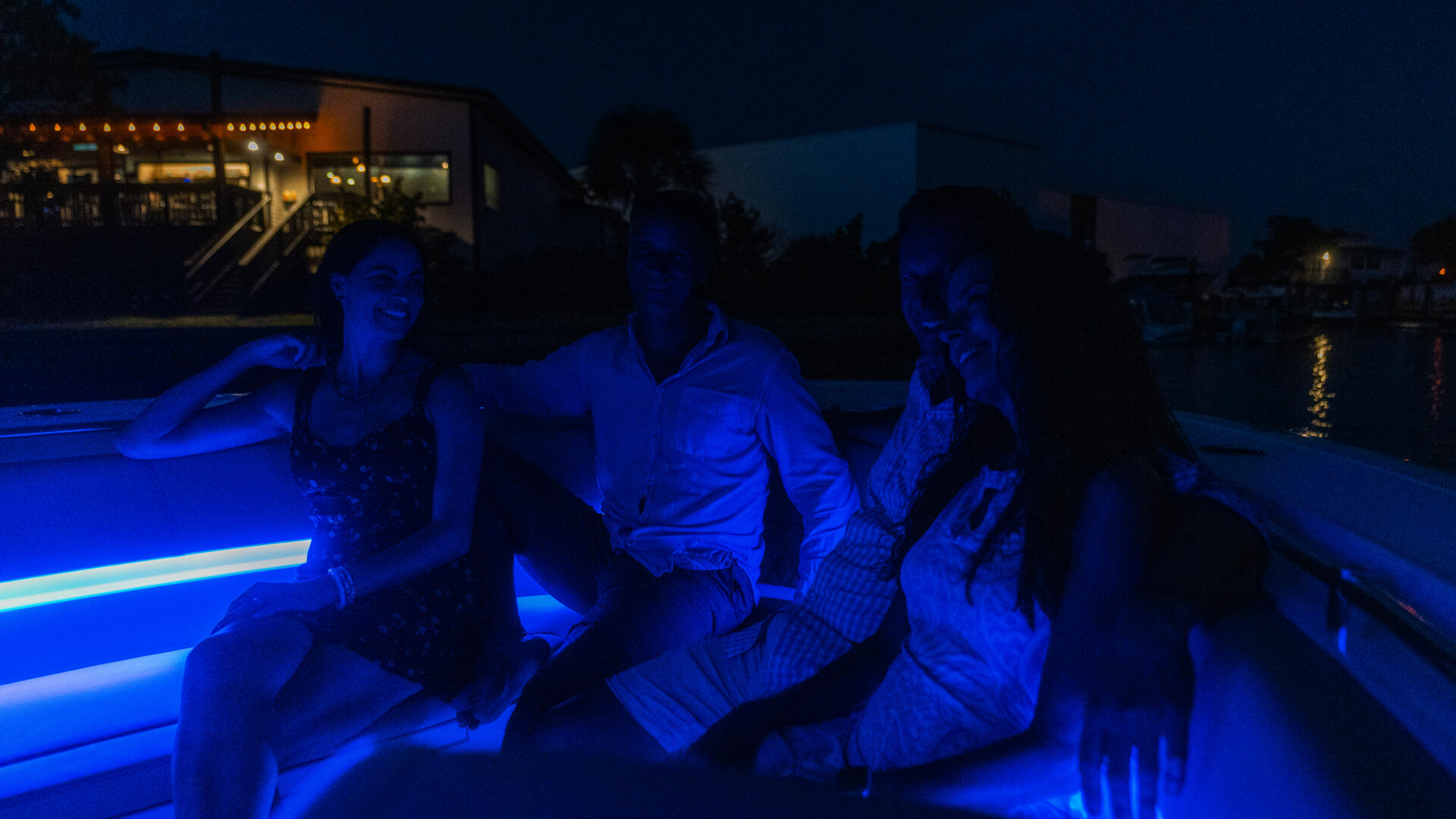 Group of people relaxing on a boat deck illuminated by blue ambient lighting at dusk