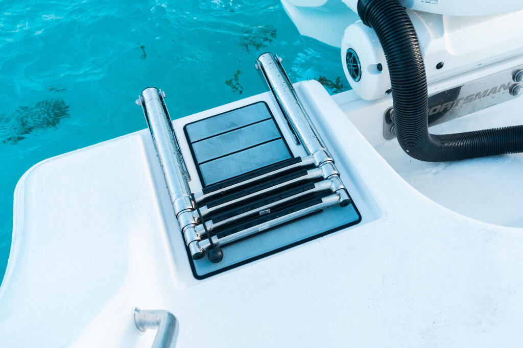 Stainless steel boarding ladder with non-slip treads mounted on white boat hull above turquoise water
