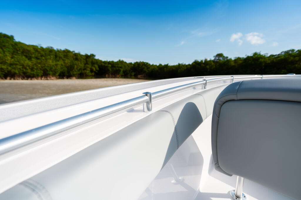 White boat gunwale and railing with mangrove shoreline and beach in background under clear blue sky