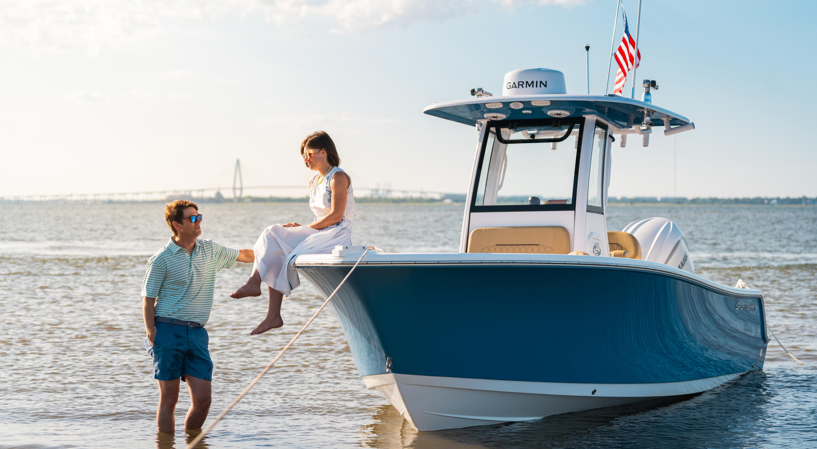 Family wading in shallow water next to a blue and white center console boat with Garmin electronics and American flag
