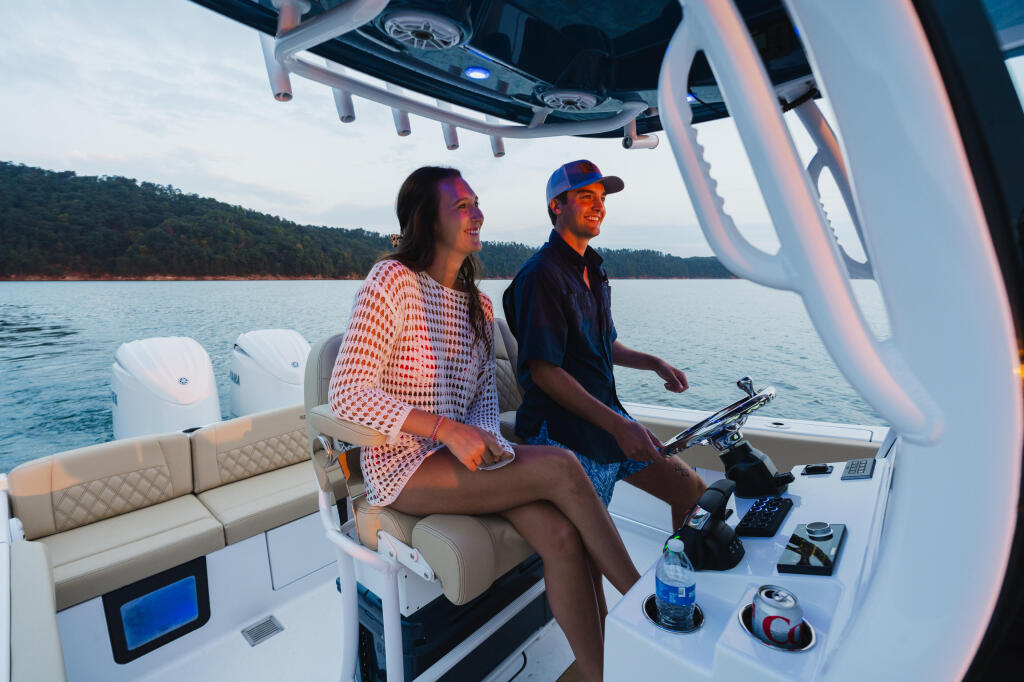 Couple relaxing at the helm of a center console boat on calm water with forested shoreline in background