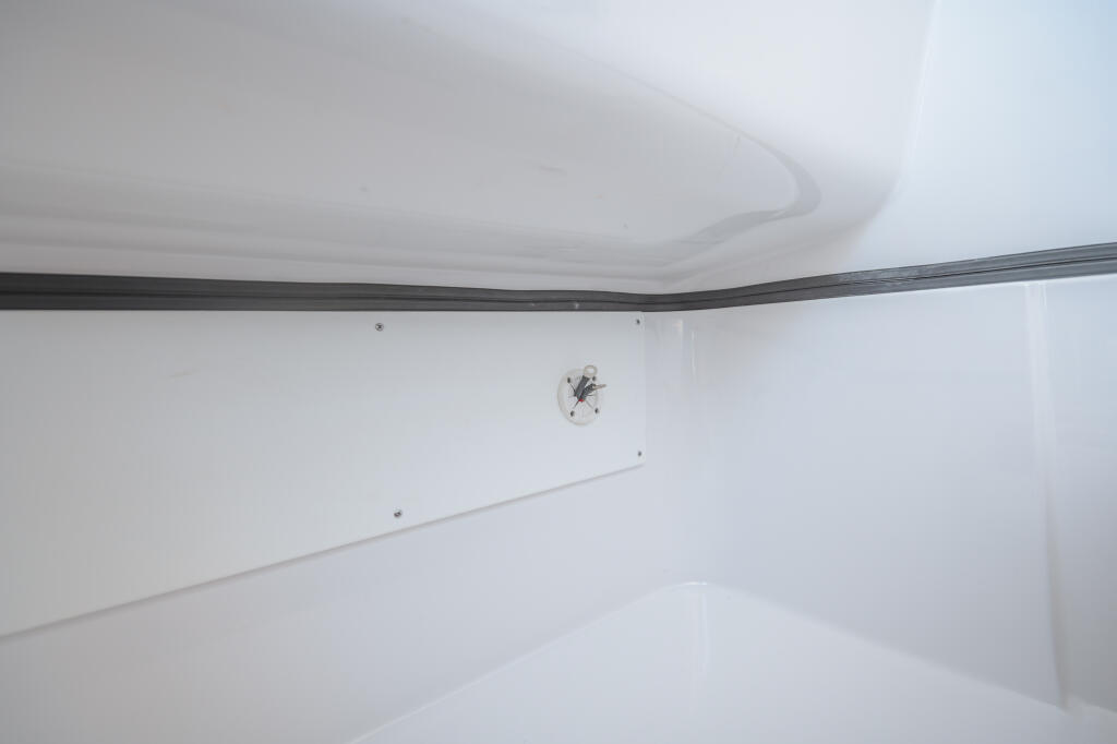 Interior cabin storage compartment with white walls, dark trim rail, and ventilation opening