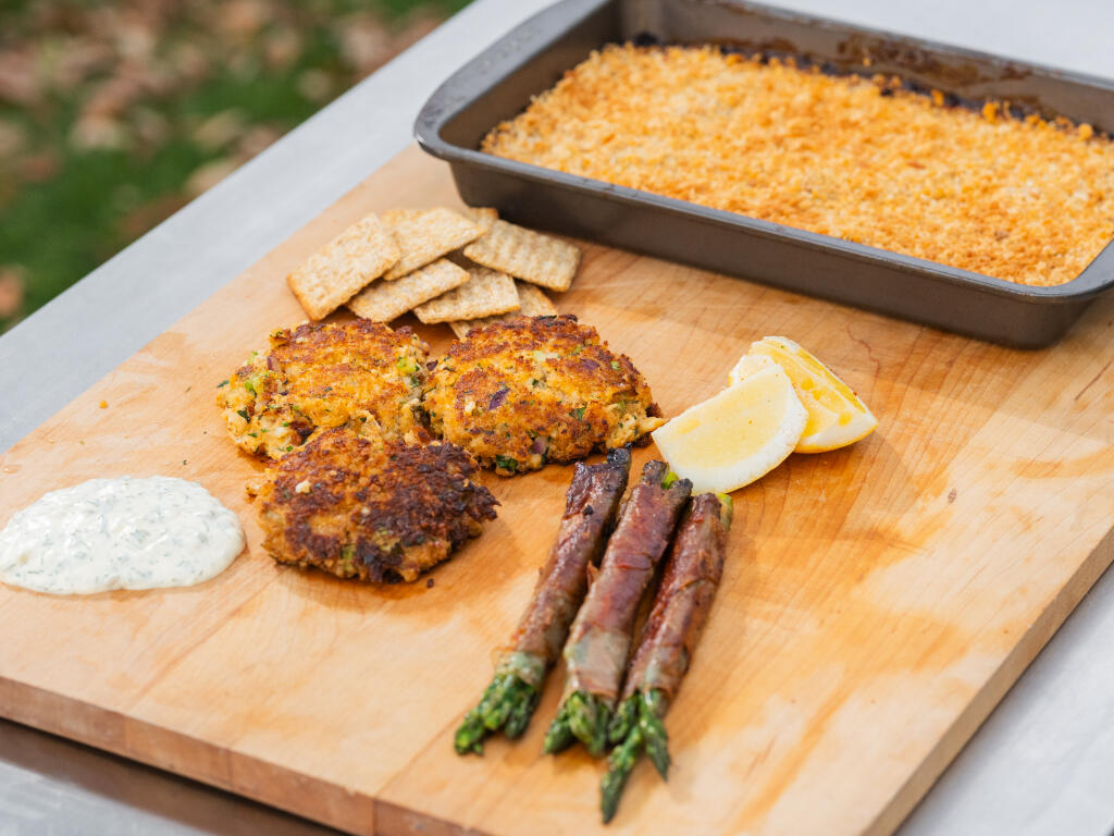 Crab cakes with asparagus, lemon, dipping sauce, and cornbread mix on a wooden cutting board
