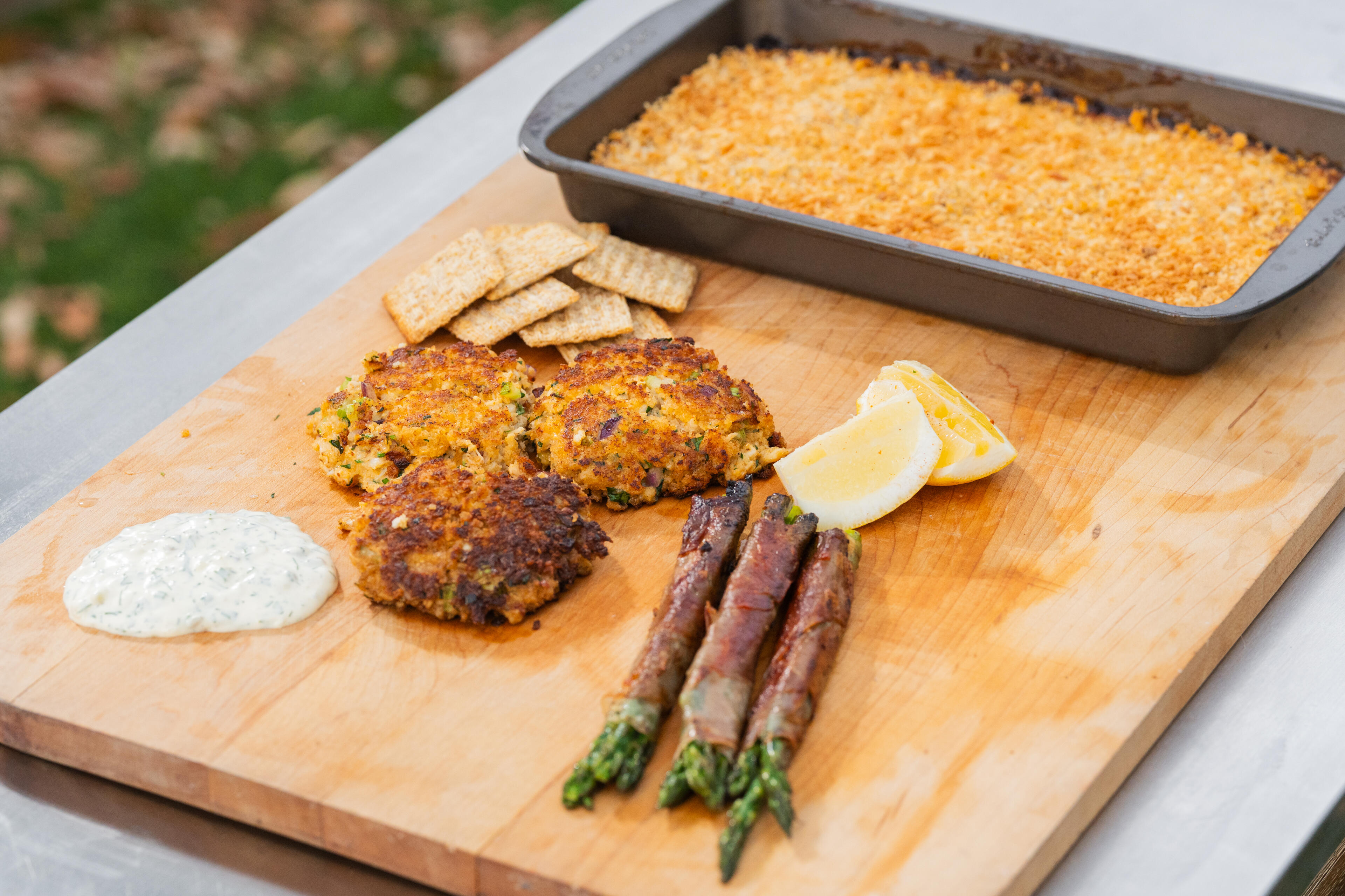 Crab cakes with asparagus, lemon, dipping sauce, and cornbread mix on a wooden cutting board