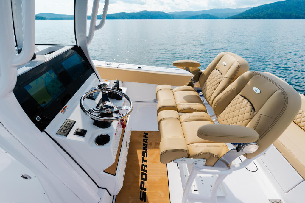Helm station with touchscreen display, steering wheel, and tan leather seating overlooking a pristine lake and forested mountains