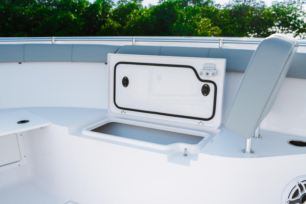 Open livewell with white lid and control panel on boat deck with gray seating and green treeline behind
