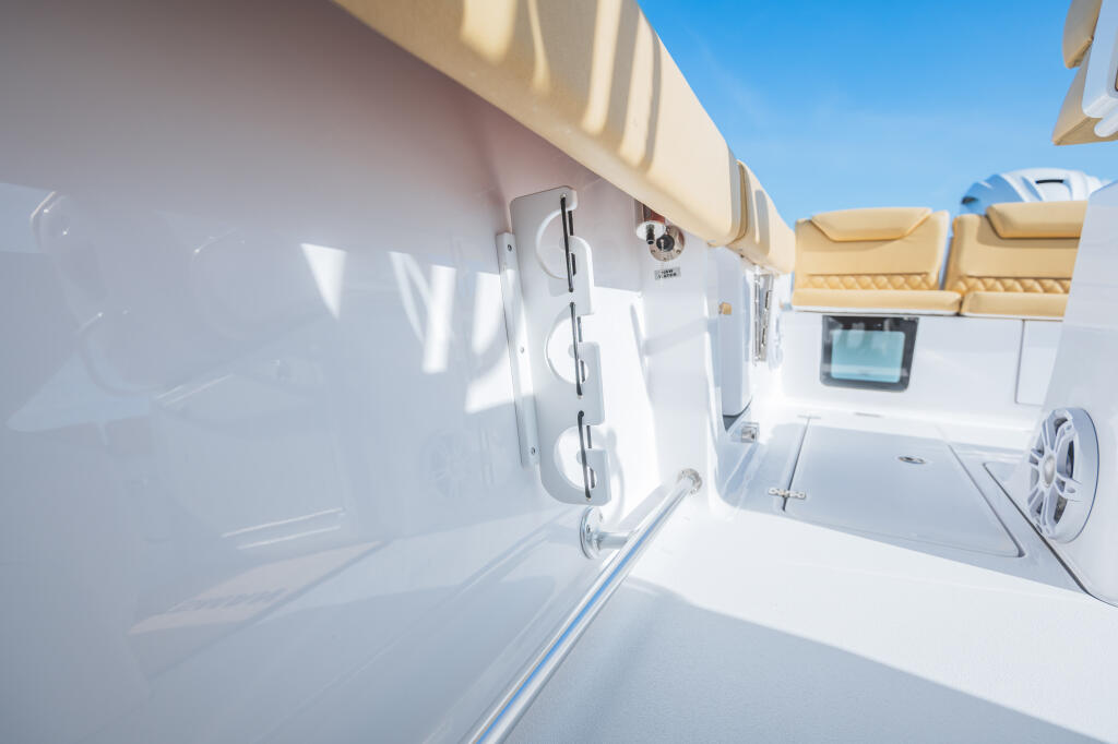 White center console boat with tan canvas canopy showing rod racks, helm electronics, and storage under clear blue sky