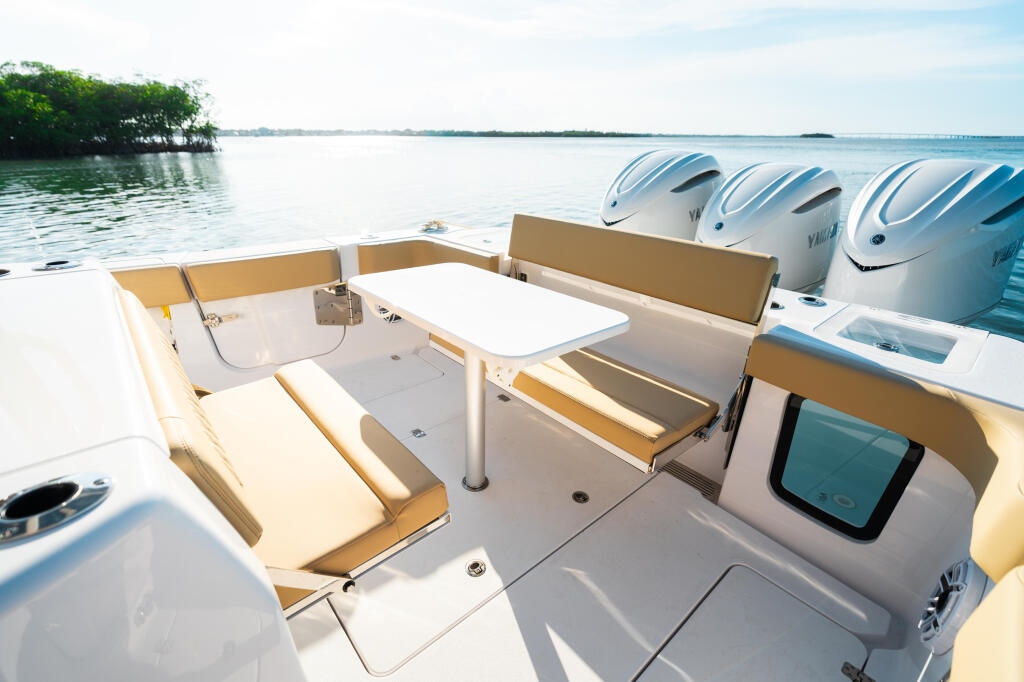 Spacious boat cabin with tan seating, white table, and triple outboard engines at the stern