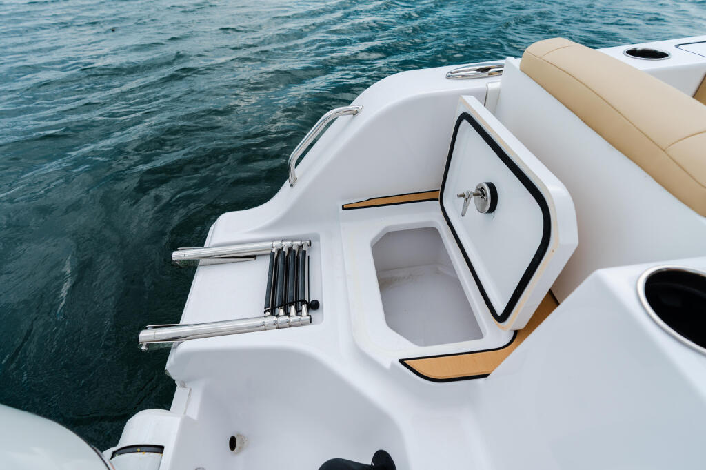 Boat's helm with steering wheel, control levers, and tan seating beside clear turquoise water