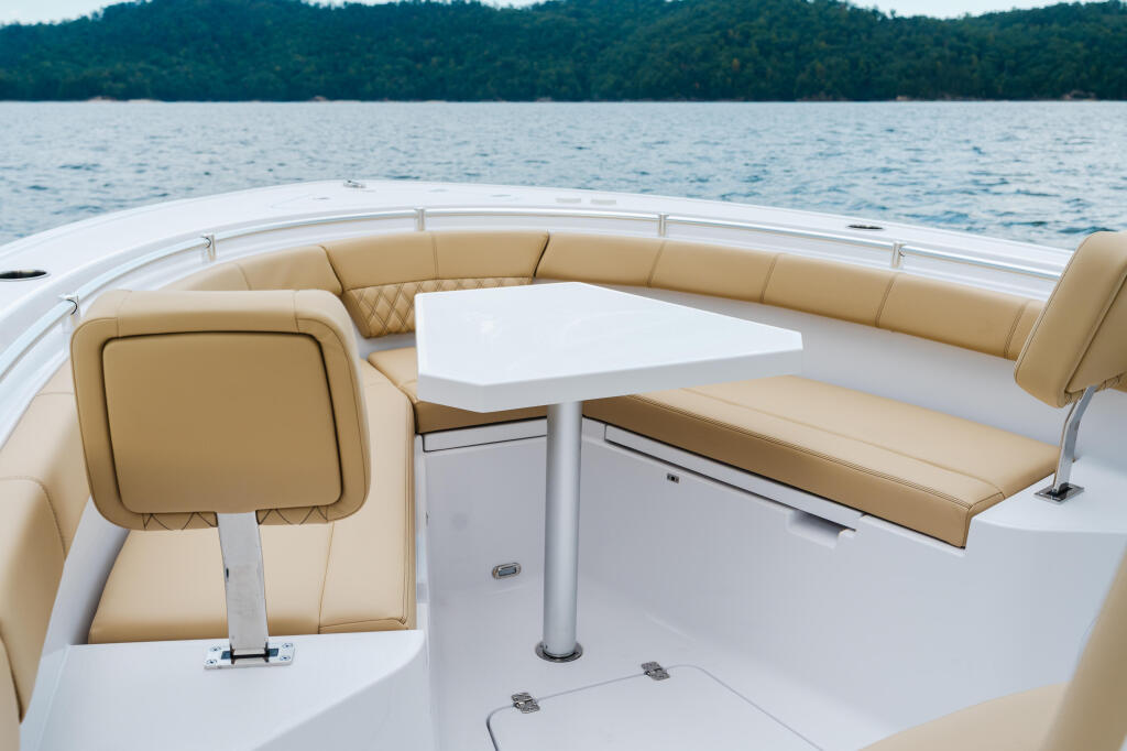 Tan leather seating and white table in a boat's cabin with forested shoreline beyond