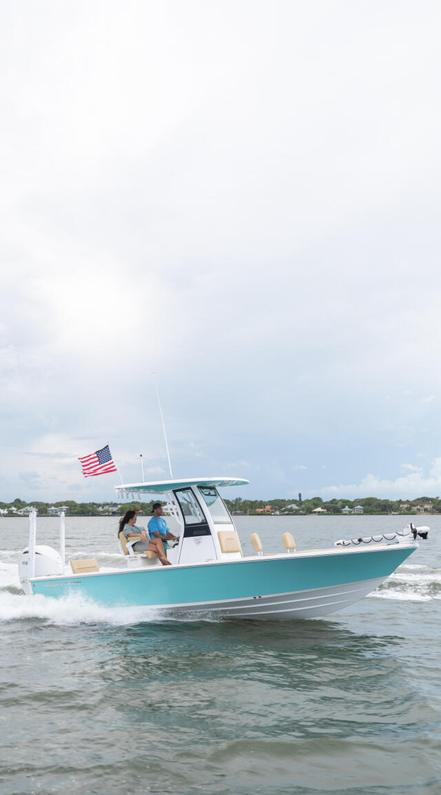 Turquoise and white center console boat running through shallow water near beach with two people aboard and American flag flying
