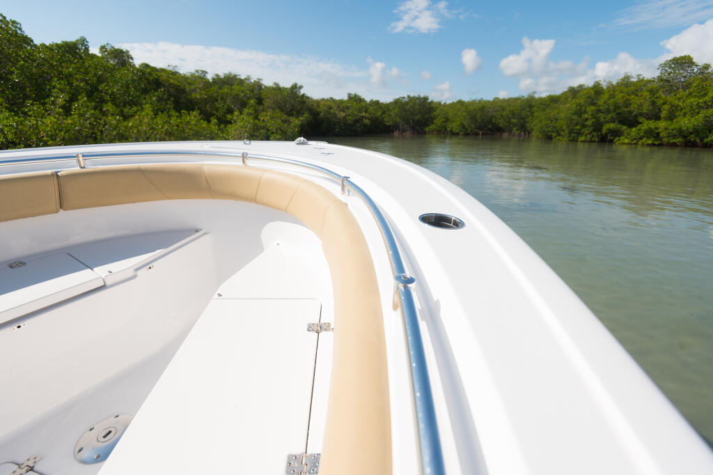 Center console bow area with tan seating and white fiberglass alongside a mangrove waterway