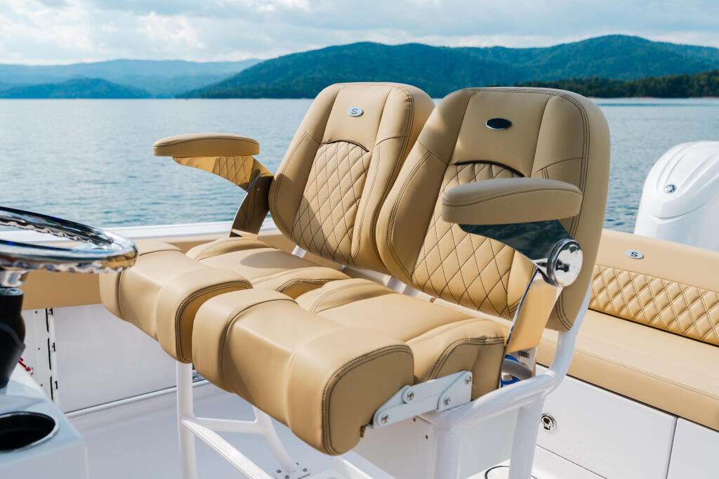 Tan leather captain's chairs with quilted detailing on a boat deck overlooking forested mountains and calm lake waters