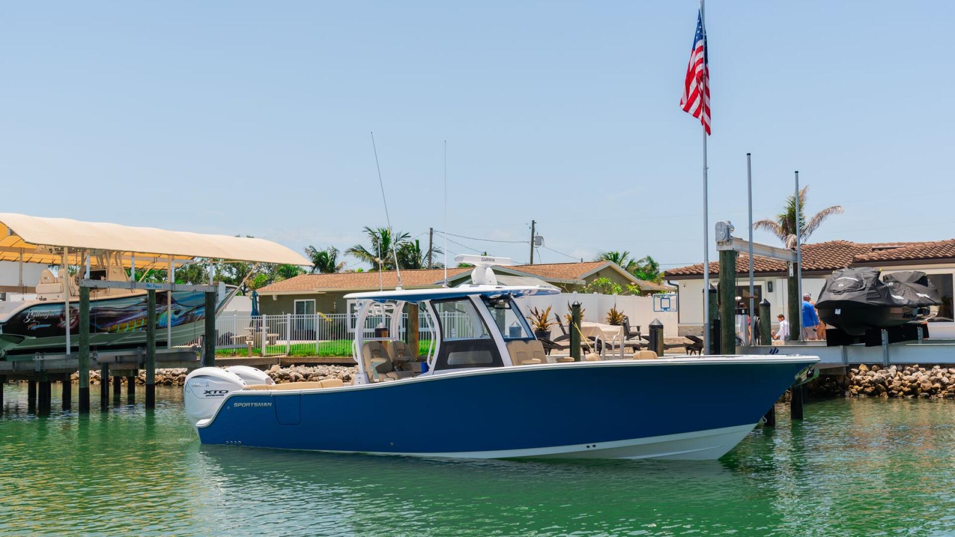 Blue and white center console boat docked at a marina with palm trees and American flag visible in background