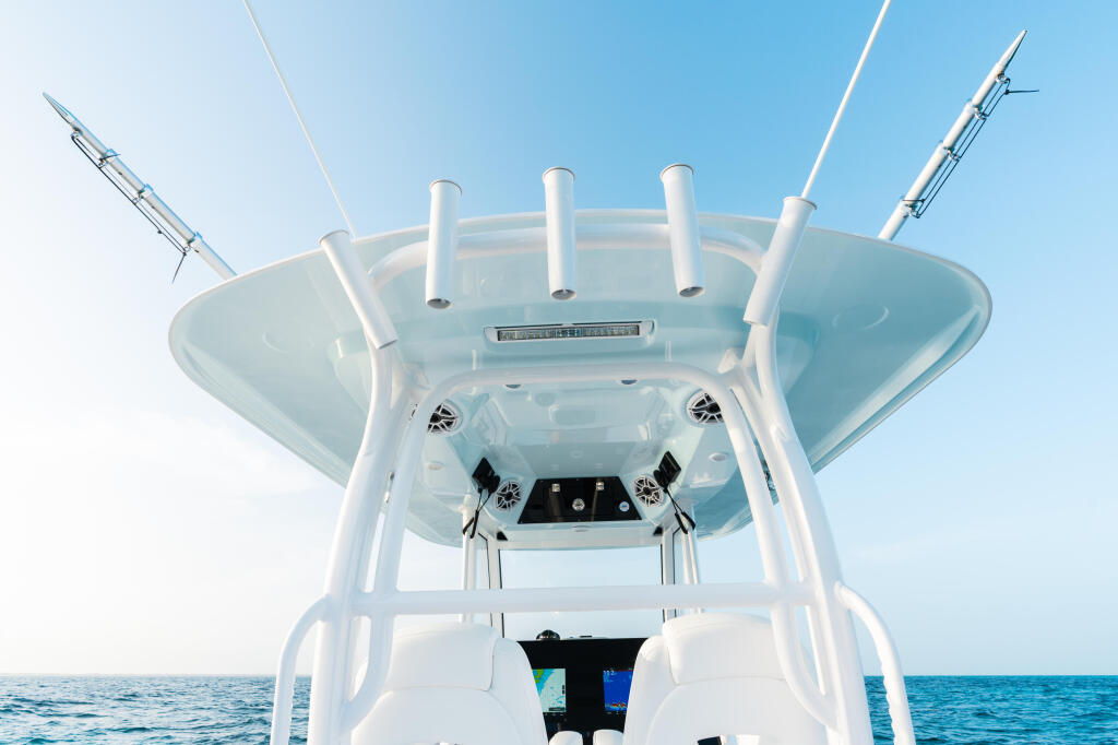 Center console fishing boat's hard-top with rod holders, antennas, and helm controls viewed from stern against clear blue sky and water