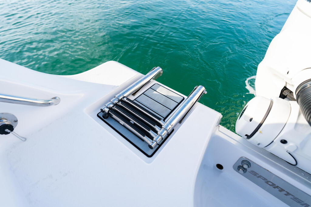 Transom detail of white sport fishing boat showing stainless steel railings and cleats above turquoise water