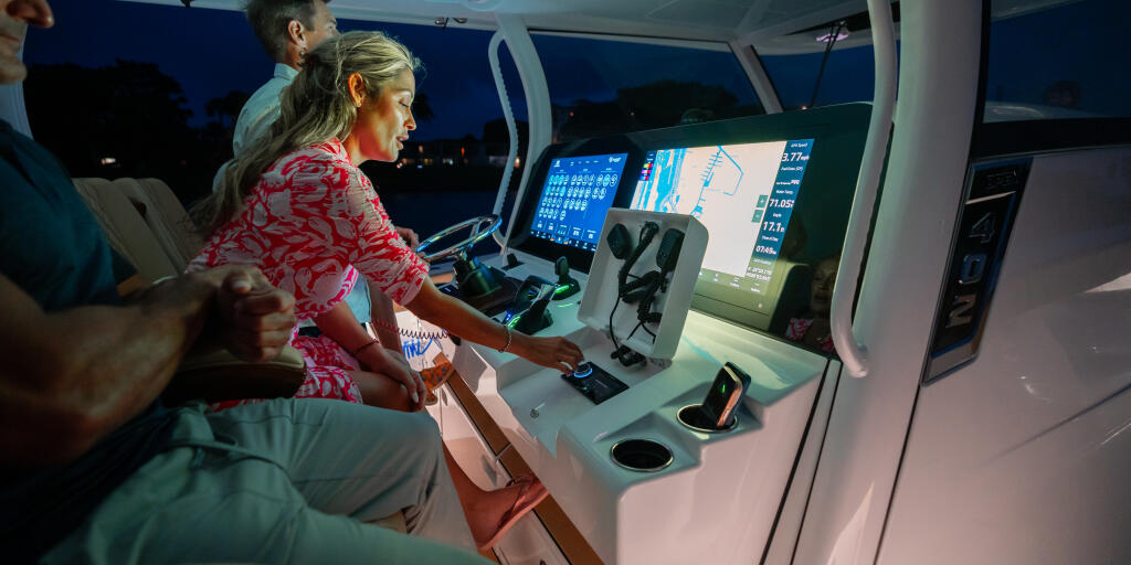 Couple at the helm of a boat at dusk, woman at controls with multiple display screens showing navigation data