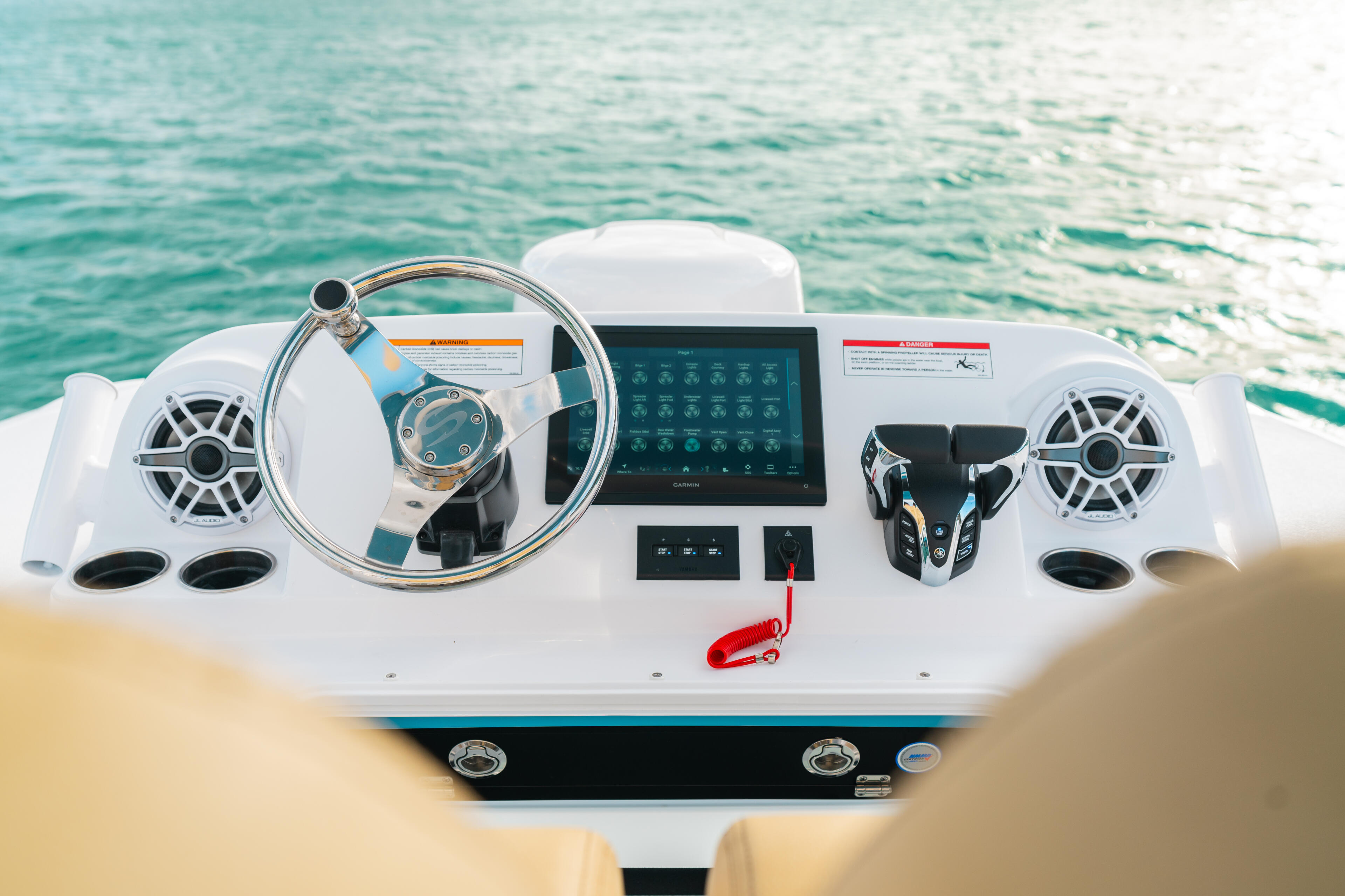 Overhead view of boat helm with steering wheel, touchscreen display, audio speakers, and control panels overlooking turquoise water
