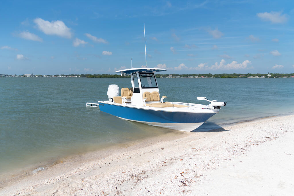 Blue and white center console boat with tan seating beached on sandy shoreline with clear shallow water
