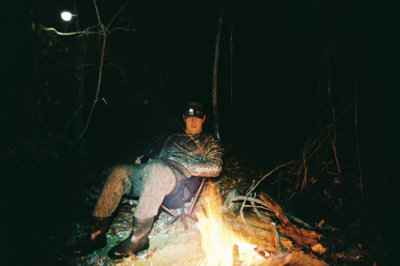 Angler holding a large striped bass by a nighttime campfire in the woods