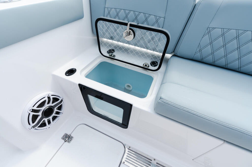 Boat cabin interior with light blue upholstered seating, white sink with mirror, speaker, and electronics display